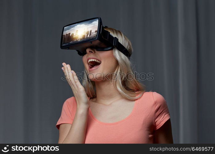 technology, augmented reality, entertainment and people concept - happy young woman with virtual headset or 3d glasses playing video game with singapore city on screen in dark room. woman in virtual reality headset or 3d glasses