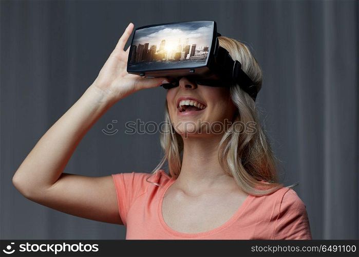 technology, augmented reality, entertainment and people concept - happy young woman with virtual headset or 3d glasses playing video game with singapore city on screen in dark room. woman in virtual reality headset or 3d glasses. woman in virtual reality headset or 3d glasses