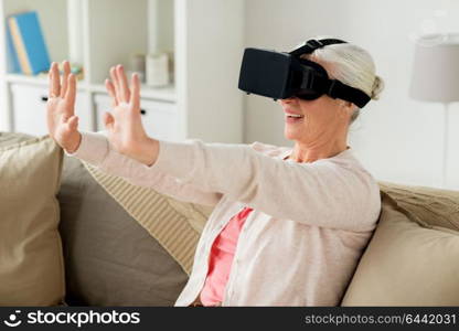 technology, augmented reality, entertainment and people concept - senior woman with virtual headset or 3d glasses playing videogame at home. old woman in virtual reality headset or 3d glasses