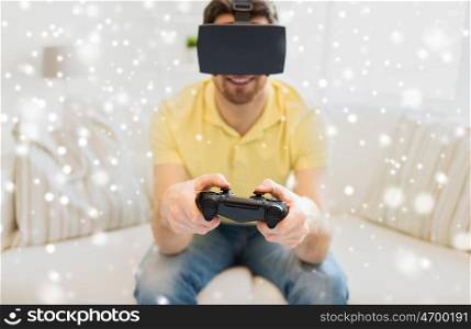 technology, augmented reality, gaming, entertainment and people concept - happy young man with virtual headset or 3d glasses playing video game with controller gamepad at home over snow