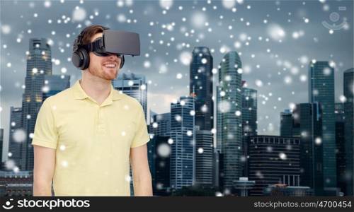 technology, augmented reality, winter, christmas and people concept - happy young man with virtual headset or 3d glasses over singapore city skyscrapers background and snow