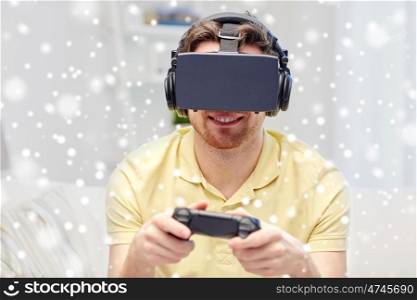 technology, augmented reality, winter, christmas and people concept - happy young man with virtual headset or 3d glasses playing video game with controller gamepad at home over snow