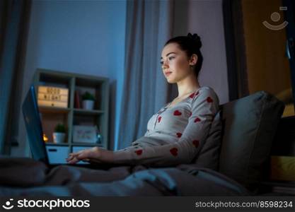 technology, bedtime and people concept - teenage girl with laptop computer sitting in bed at home at night. teenage girl with laptop in bed at home at night