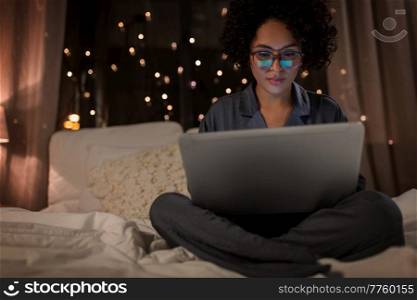 technology, bedtime and rest concept - woman in pajamas with laptop computer working in bed at night. woman with laptop working in bed at night