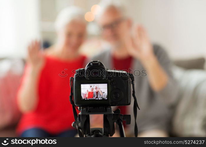 technology, blogging and people concept - happy smiling senior couple with camera recording video message or taking picture at home. happy senior couple with camera recording video