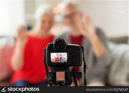 technology, blogging and people concept - happy smiling senior couple with camera recording video message or taking picture at home. happy senior couple with camera recording video
