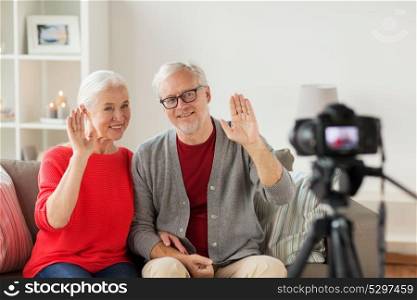 technology, blogging and people concept - happy smiling senior couple with camera recording video message or taking picture at home. happy senior couple with camera recording video