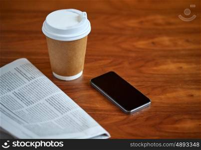 technology, break, mass media and news concept - coffee drink in paper cup, smartphone and newspaper on table