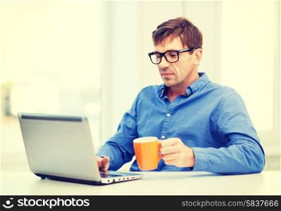 technology, business and lifestyle concept - man in eyeglasses working with laptop at home, holding a cup of warm tea or coffee