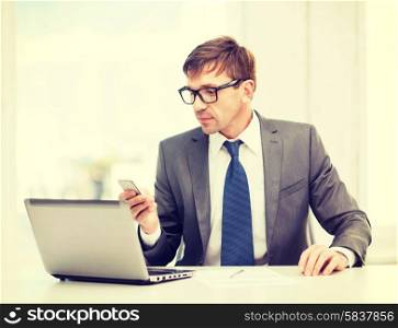 technology, business and office concept - handsome businessman working with laptop computer and smartphone