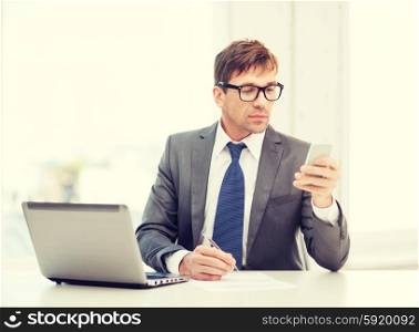 technology, business and office concept - handsome businessman working with laptop computer and smartphone