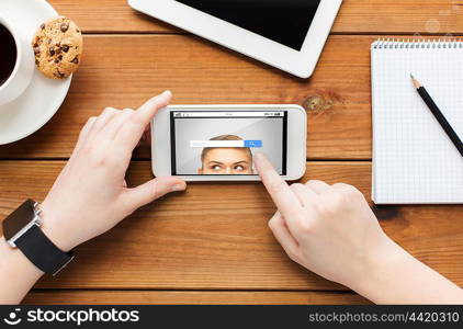 technology, business and people concept - close up of woman with internet search browser on smartphone screen and coffee cup on wooden table