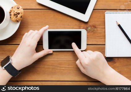 technology, business, communication, people and advertisement concept - close up of woman with blank smartphone screen and coffee cup on wooden table