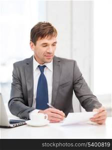 technology, business, education and office concept - handsome businessman working with laptop computer and documents