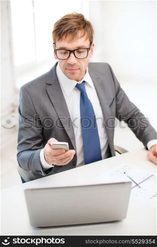 technology, business, internet and office concept - handsome businessman working with laptop computer and smartphone