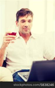 technology, business, leisure, drinks, retirement and lifestyle concept - happy man with laptop computer and glass of rose wine at home