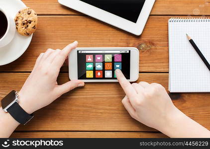 technology, business, media and people concept - close up of woman hands with menu icons on smartphone screen and coffee cup on wooden table