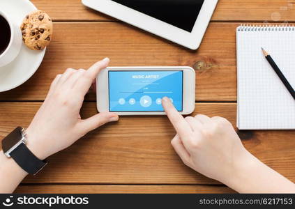 technology, business, multimedia and people concept - close up of woman with music player application smartphone screen and coffee cup on wooden table