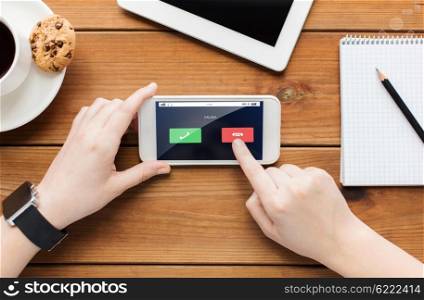 technology, business, people and communication concept - close up of woman with incoming call on smartphone screen and coffee cup on wooden table