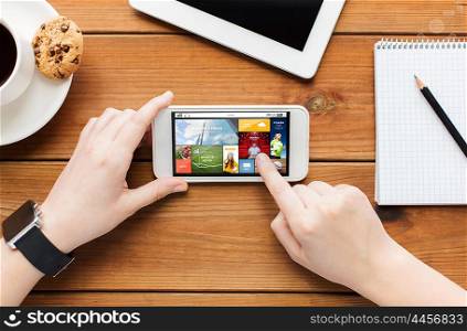 technology, business, people and media concept - close up of woman with news application on smartphone screen and coffee cup on wooden table