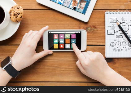 technology, business, people and media concept - close up of woman with menu icons on smartphone screen and coffee cup on wooden table