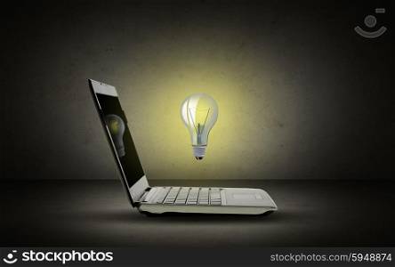 technology, business, startup and idea concept - open laptop computer with lighting bulb over dark gray background