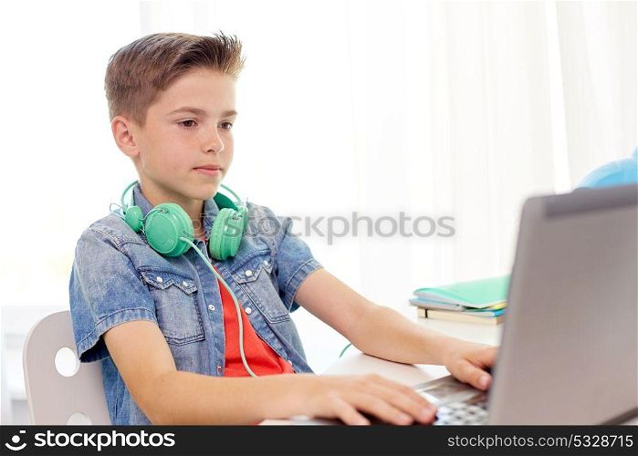 technology, childhood and people concept - happy boy with headphones typing on laptop computer at home. happy boy with headphones typing on laptop at home