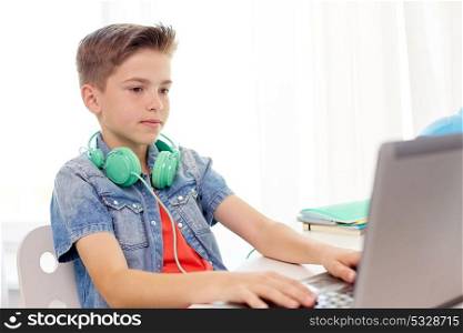 technology, childhood and people concept - happy boy with headphones typing on laptop computer at home. happy boy with headphones typing on laptop at home
