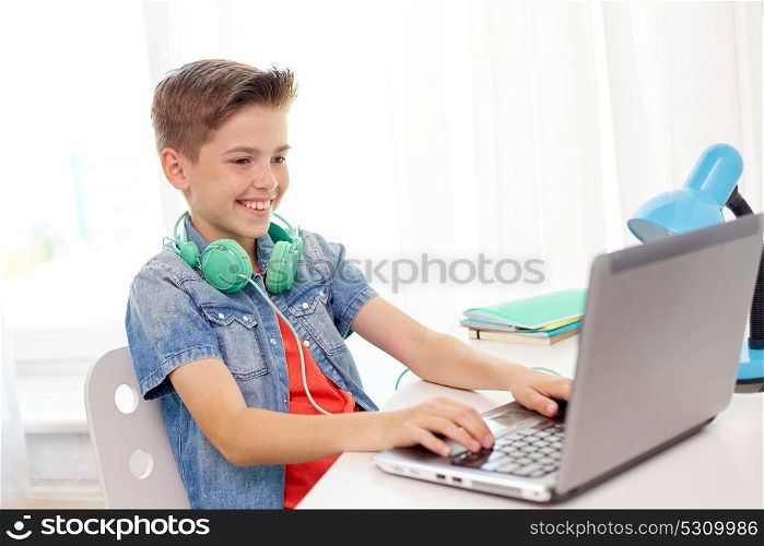 technology, childhood and people concept - happy smiling boy with headphones typing on laptop computer at home. happy boy with headphones typing on laptop at home