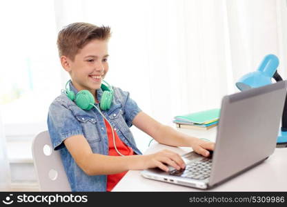 technology, childhood and people concept - happy smiling boy with headphones typing on laptop computer at home. happy boy with headphones typing on laptop at home