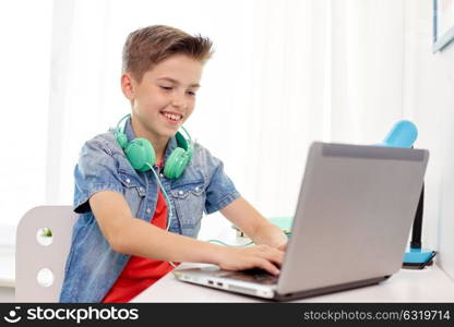 technology, childhood and people concept - happy smiling boy with headphones typing on laptop computer at home. happy boy with headphones typing on laptop at home