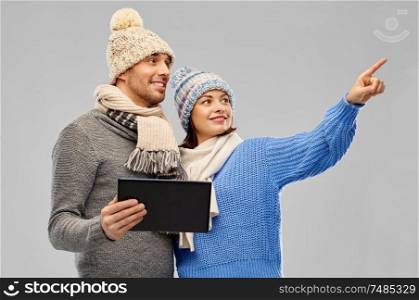 technology, christmas and winter clothes concept - happy couple in knitted hats and scarves with tablet computer over grey background. couple in winter clothes with tablet computer