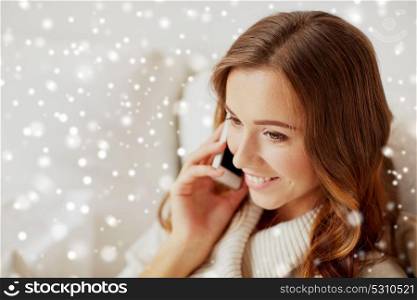 technology, christmas, communication and people concept - happy young woman calling on smartphone at home with snow. happy young woman calling on smartphone at home