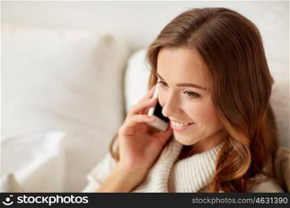 technology, christmas, communication and people concept - happy young woman calling on smartphone at home
