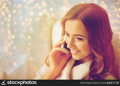 technology, christmas, communication and people concept - happy young woman calling on smartphone at home. happy young woman calling on smartphone at home