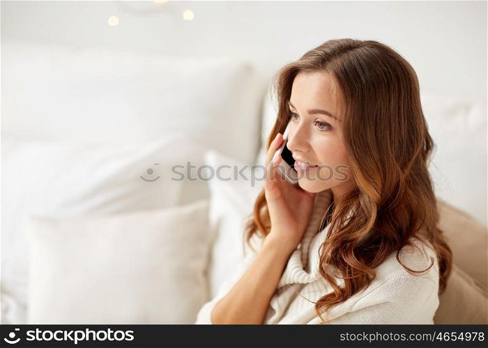 technology, christmas, communication and people concept - happy young woman calling on smartphone at home bedroom