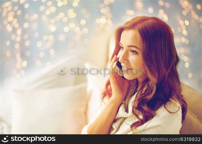 technology, christmas, communication and people concept - happy young woman calling on smartphone at home bedroom. happy young woman calling on smartphone at home