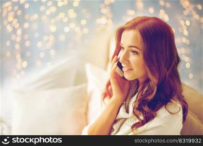 technology, christmas, communication and people concept - happy young woman calling on smartphone at home bedroom. happy young woman calling on smartphone at home