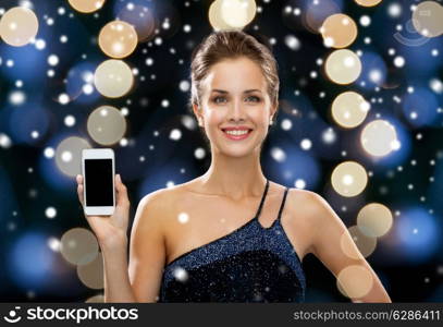 technology, christmas, holidays, advertising and people concept - smiling woman in evening dress holding smartphone over night lights and snow background