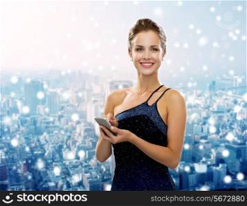 technology, christmas, holidays and people concept - smiling woman in evening dress holding smartphone over snowy city background