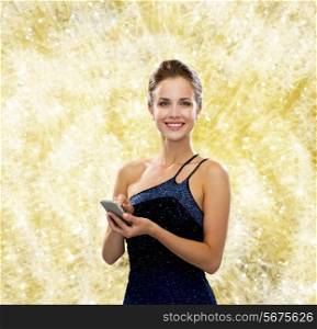 technology, christmas, holidays and people concept - smiling woman in evening dress holding smartphone over yellow holidays lights background