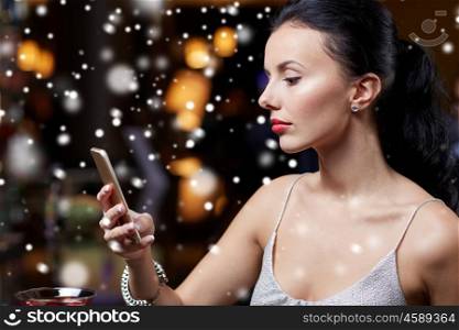 technology, christmas, winter holidays and people concept - young woman texting on smartphone at night club or bar over snow