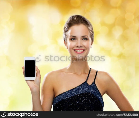 technology, communication, advertisement and people concept - smiling woman in evening dress holding smartphone over yellow holidays lights background