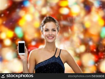 technology, communication, advertisement and people concept - smiling woman in evening dress holding smartphone over red holidays lights background