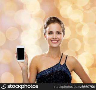 technology, communication, advertisement and people concept - smiling woman in evening dress holding smartphone over holidays lights background