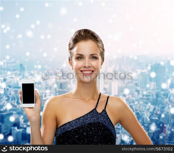 technology, communication, advertising and people concept - smiling woman in evening dress showing smartphone blank screen over snowy city background