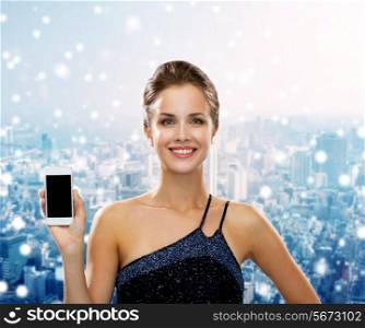 technology, communication, advertising and people concept - smiling woman in evening dress showing smartphone blank screen over snowy city background