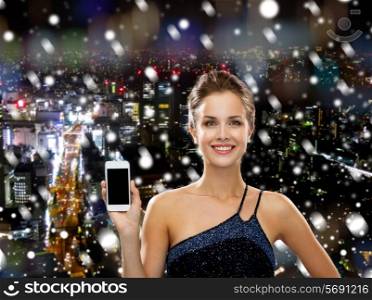 technology, communication, advertising and people concept - smiling woman in evening dress showing smartphone blank screen over snowy night city background