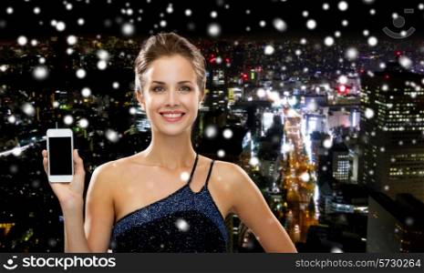 technology, communication, advertising and people concept - smiling woman in evening dress holding smartphone over snowy night city background