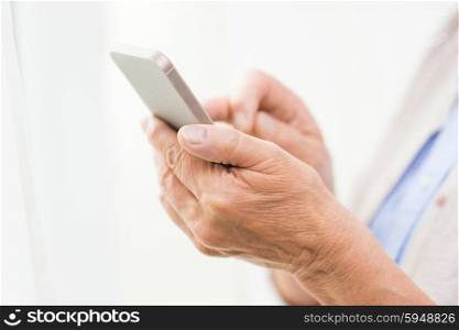technology, communication age and people concept - close up of senior woman hands with smartphone texting message at home